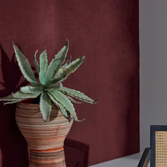 Een plant in een aardetinten pot staat voor een donkerrood Elitis Parthenon RM 1045 70 Rayures Jumelles behang.