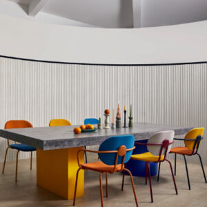 Moderne eetkamer met kleurrijke stoelen, een betonnen tafel en Elitis Pilastre RM 1043 01 en Colonne RM 1044 01 Rayures Jumelles behang op de achtergrond.