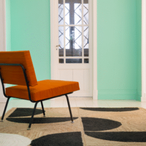 Oranje stoel op een Elitis Rocky vloerkleed met zwart patroon in een mintgroene kamer.