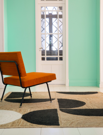 Oranje stoel op een Elitis Rocky vloerkleed met zwart patroon in een mintgroene kamer.
