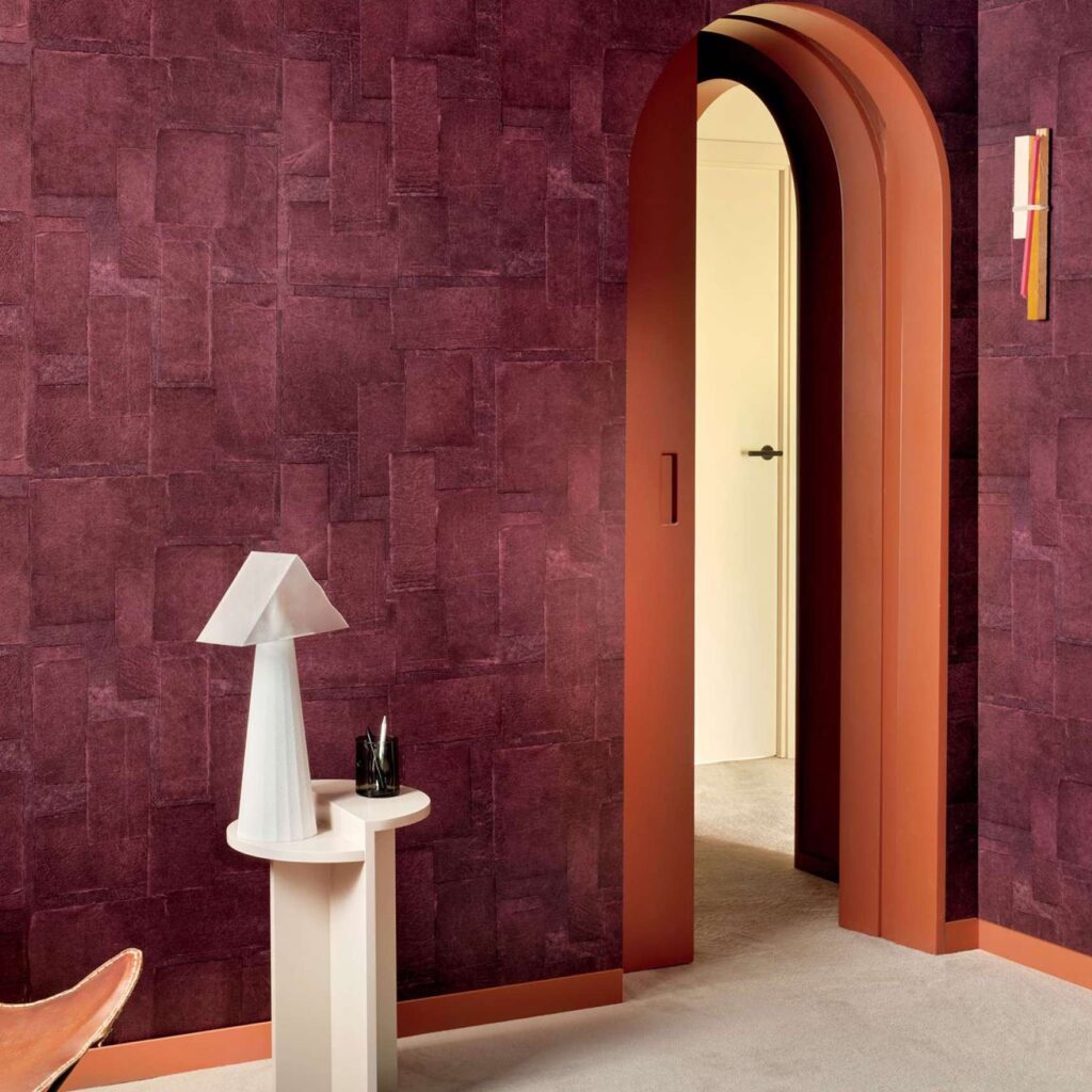Moderne interieurhoek met Elitis Sangpi VP 1018-39 behang in dieprode tint, een boogdeur en een designlamp op een wit tafeltje.