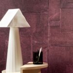 Moderne interieursetting met Elitis Sangpi VP 1018-39 paarse textuurbehang op de muur en een witte designlamp op een beige bijzettafel.
