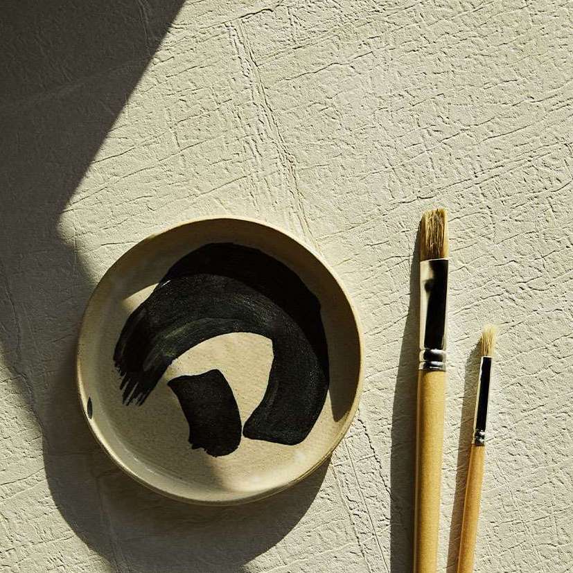 Beige Elitis Sangpi VP 1018 60 behang met voelbare textuur, naast een penseelbord en twee kwasten.