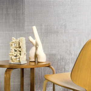 Houten bijzettafel met abstracte sculpturen en een houten stoel, tegen een Elitis Silver wandbekleding.