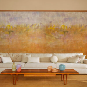 Luxe woonkamer met een groot Elitis Solstice VP 966 01 atelier d'artiste behang in warme aardetinten achter een moderne, lichte bank.