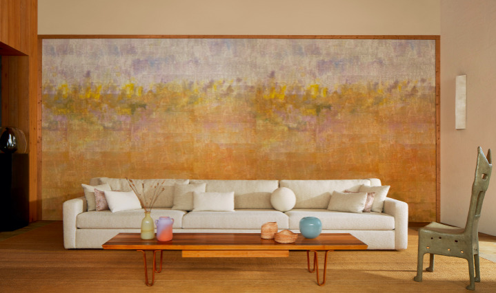 Luxe woonkamer met een groot Elitis Solstice VP 966 01 atelier d'artiste behang in warme aardetinten achter een moderne, lichte bank.