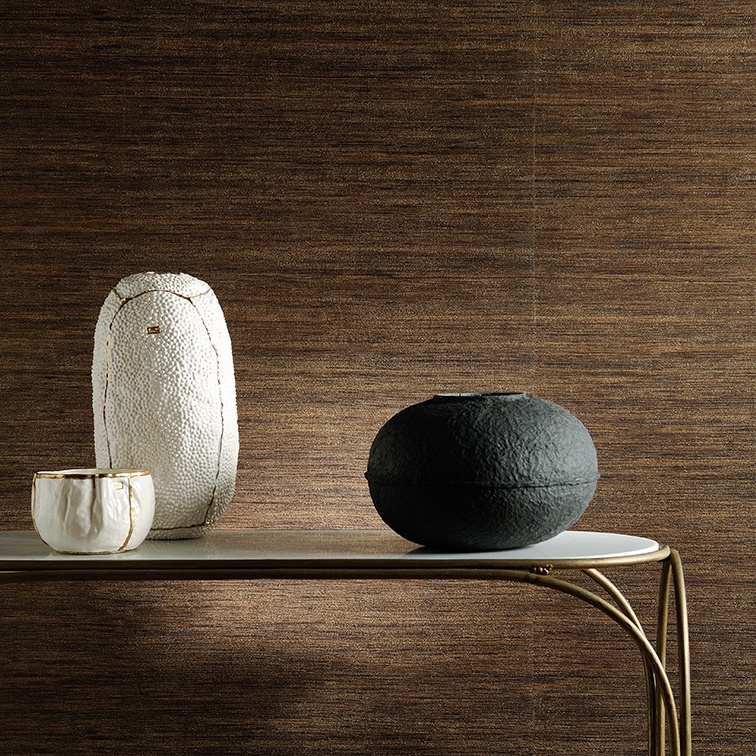 Decoratieve objecten op een tafel voor een luxe Elitis Talamone Seta wandbekleding in warme bruintinten.