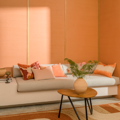 Moderne woonkamer met Elitis Tribus sisal muurafwerking in warme perzikkleur, een lichtgrijze bank met sierkussens en een houten salontafel met vaas.