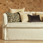 Witte Elitis Aimee CO 261 bank van Buningh met decoratieve kussens in neutrale en donkere tinten tegen een stenen muur.