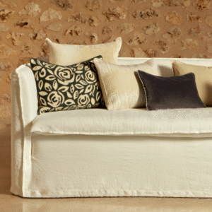 Witte Elitis Aimee CO 261 bank van Buningh met decoratieve kussens in neutrale en donkere tinten tegen een stenen muur.