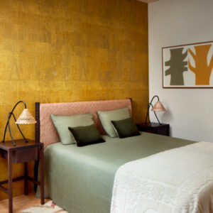 Sfeervolle slaapkamer met Elitis Atelier d’artiste VP 880 28 behang in goudtint achter het bed.