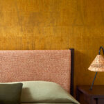 Detail van een slaapkamer met Elitis Atelier d’artiste VP 880 28 behang in warme aardetint en een stoffen hoofdbord.
