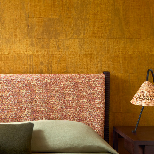 Detail van een slaapkamer met Elitis Atelier d’artiste VP 880 28 behang in warme aardetint en een stoffen hoofdbord.