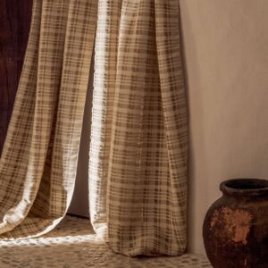 Lichtdoorlatend Elitis Baleares Brisa CN 004 29 gordijn met beige ruitpatroon in een rustieke interieursetting.