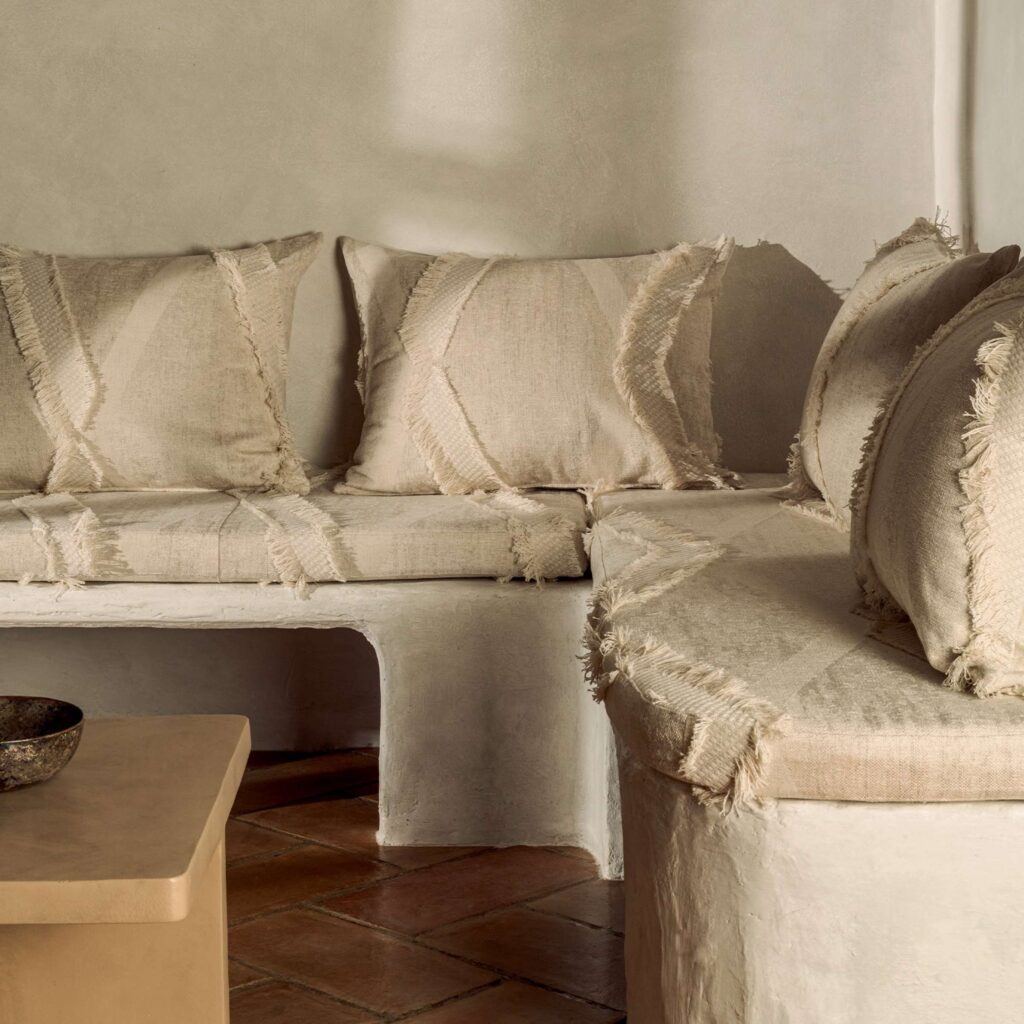 Rustieke zithoek met Elitis Baleares Duna stof in beige tinten en franje-afwerking op kussens en bekleding.