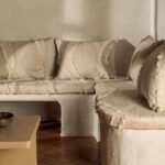 Rustieke zithoek met Elitis Baleares Duna stof in beige tinten en franje-afwerking op kussens en bekleding.