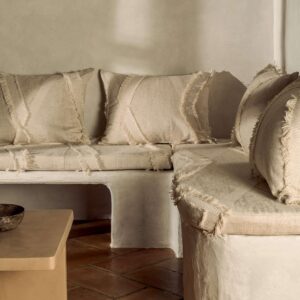Rustieke zithoek met Elitis Baleares Duna stof in beige tinten en franje-afwerking op kussens en bekleding.