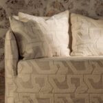 Beige Elitis Baleares Eivissa LR 370 01 bank met bijpassende kussens in een geometrisch patroon tegen een rustieke stenen muur.