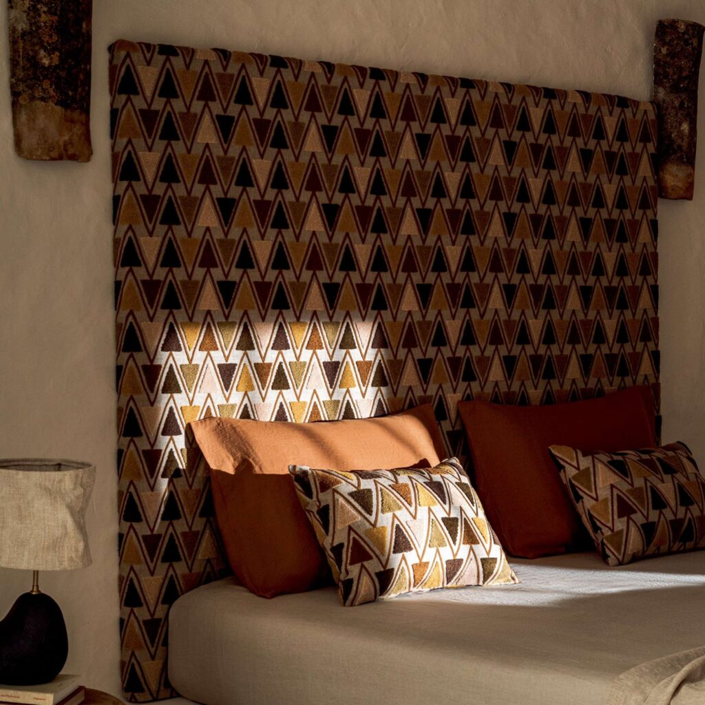 Bed met kussens en een groot Elitis Baleares Joya LZ 904 22 hoofdbord met geometrisch patroon in warme aardetinten.