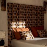 Bed met kussens en een groot Elitis Baleares Joya LZ 904 22 hoofdbord met geometrisch patroon in warme aardetinten.