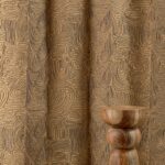 Beige Elitis Baleares Llenya LZ 905 01 gordijn met abstract patroon en houten decoratief object op de voorgrond.