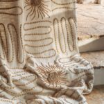 Crèmekleurige Elitis Baleares Paloma LZ 898 01 stof met zon- en lijnpatronen in reliëf, gedrapeerd over een natuurstenen trap.