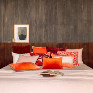 Sierkussens in warme oranjetinten, waaronder het Elitis Basile Co 257 34 02 kussen, liggen op een opgemaakt bed in een sfeervolle slaapkamer.