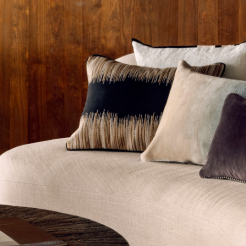 Modern sierkussen Elitis Basile CO 257 89 02 op een beige gebogen bank voor een houten muur.