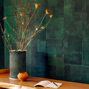 Groene muur met Elitis-behang Art paper Amami RM 1035 06, met een houten tafel, vaas met gedroogde takken en een open notitieboekje.