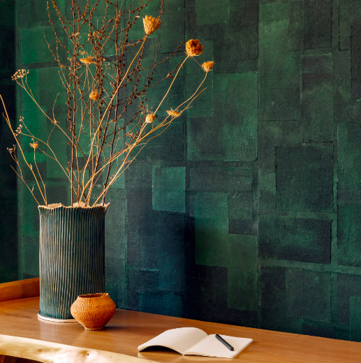 Groene muur met Elitis-behang Art paper Amami RM 1035 06, met een houten tafel, vaas met gedroogde takken en een open notitieboekje.