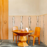 Houten tafel en stoelen in een kamer met Elitis behang ‘Naoshima RM 1031 03’ met abstracte figuren op de muur.