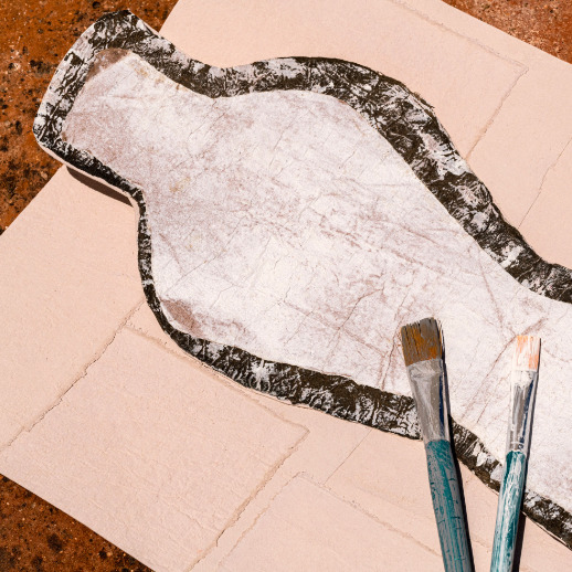 Abstracte vorm op Elitis-behang Art Paper Naoshima RM 1031 03 met twee verfkwasten erop geplaatst.