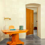Interieur met Elitis Art Paper Okinawa RM 1032 01 crèmekleurig behang, houten tafel en open houten deur.