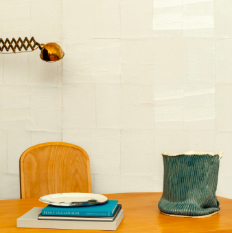 Woonkamer met Elitis Art Paper Okinawa behang, houten tafel, designlamp en decoratieve accessoires.