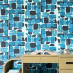 Elitis-behang Chaman met abstract blauw patroon achter een vintage bureau met een leeslamp en open boek.