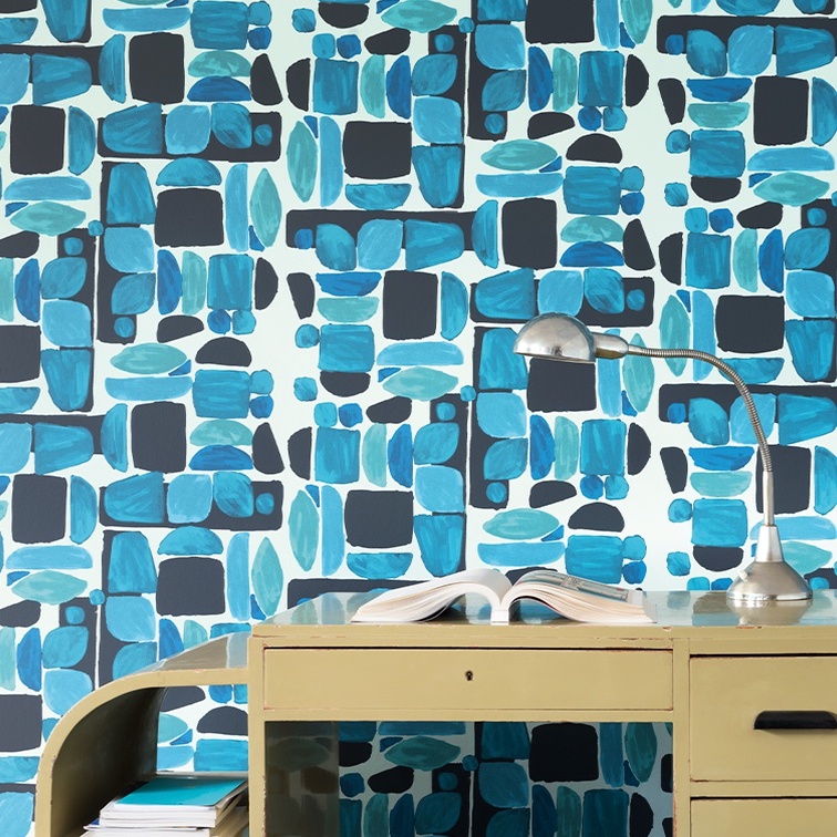 Elitis-behang Chaman met abstract blauw patroon achter een vintage bureau met een leeslamp en open boek.