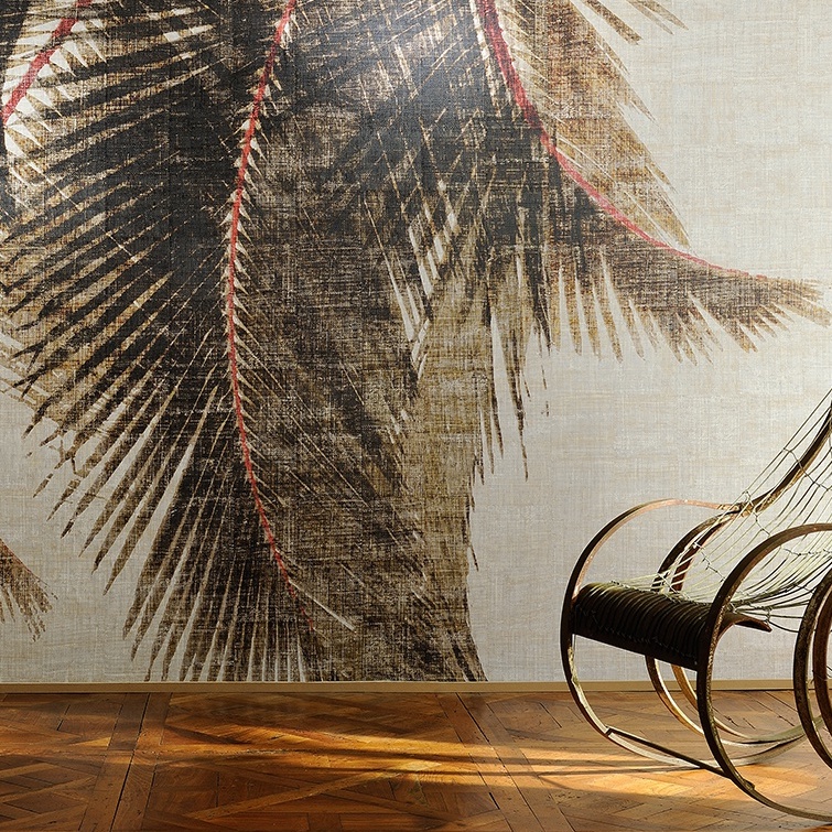 Behang uit de Elitis Cuba Libre collectie met een groot palmbladmotief en een rotan schommelstoel op een houten vloer.