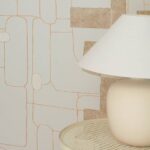 Beige tafellamp op een metalen bijzettafel voor Elitis-behang Cuzco TP 332 uit de Voile de papier-collectie.