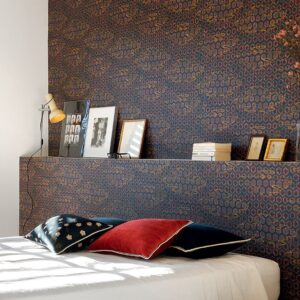 Sfeervolle slaapkamer met Elitis-behang De Lac en Lac TP 285 01 in donkerblauw met goudaccenten, een boekenplank met decoratieve lijsten en een bed met gekleurde kussens.