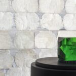 Detail van Elitis-behang Ecrin Puerto Princesa met glanzende, ronde parelmoerachtige vlakken en een groene glazen decoratie op een zwarte zuil.