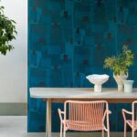 Moderne eethoek met roze stoelen en houten tafel tegen een diepblauw Elitis Espiritu TP 329 behang uit de Voile de Papier collectie.