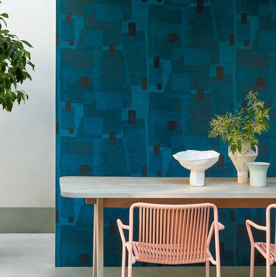 Moderne eethoek met roze stoelen en houten tafel tegen een diepblauw Elitis Espiritu TP 329 behang uit de Voile de Papier collectie.