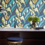 Interieur met Elitis-behang "Fleur de Lune" met kleurrijk bladmotief achter een marmeren wastafel en decoratieve accessoires.