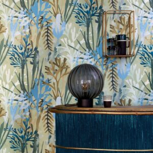Elitis-behang Flower Power Algues met abstracte zeewiertekening in blauw- en groentinten, gecombineerd met een blauwe kast en decoratieve accessoires.