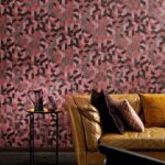 Luxe interieur met Elitis behang Formentera Juego de Paja in rood-roze geometrisch patroon achter een bruine leren bank en bijzettafeltje.