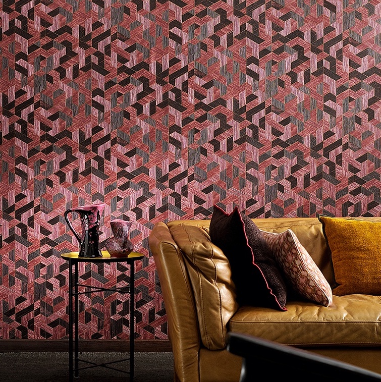 Luxe interieur met Elitis behang Formentera Juego de Paja in rood-roze geometrisch patroon achter een bruine leren bank en bijzettafeltje.