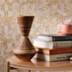 Interieurdetail met Elitis-behang Formentera Juego de paja VP 717 op de achtergrond, naast een stapel boeken, een terracotta kop-en-schotel en een decoratieve vaas op een tafel.