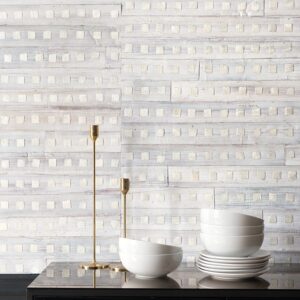 Zachte witte muur met Elitis-behang Iloilo RM 970 01 als achtergrond, met witte kommen en gouden kandelaars op een donker meubel.