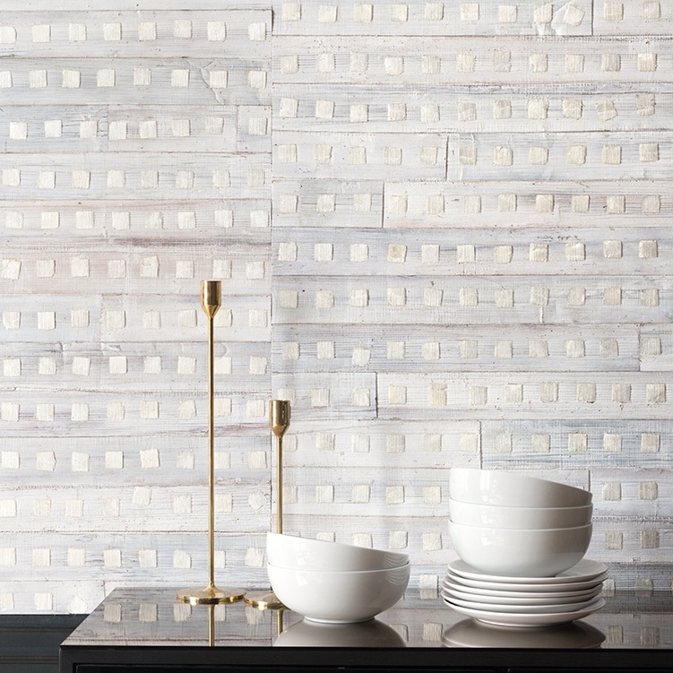 Zachte witte muur met Elitis-behang Iloilo RM 970 01 als achtergrond, met witte kommen en gouden kandelaars op een donker meubel.