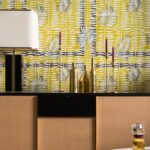 Modern interieur met Elitis-behang Initiation Mantra TP 314 04 in geelgroene tinten en decoratieve gouden accessoires op een dressoir.